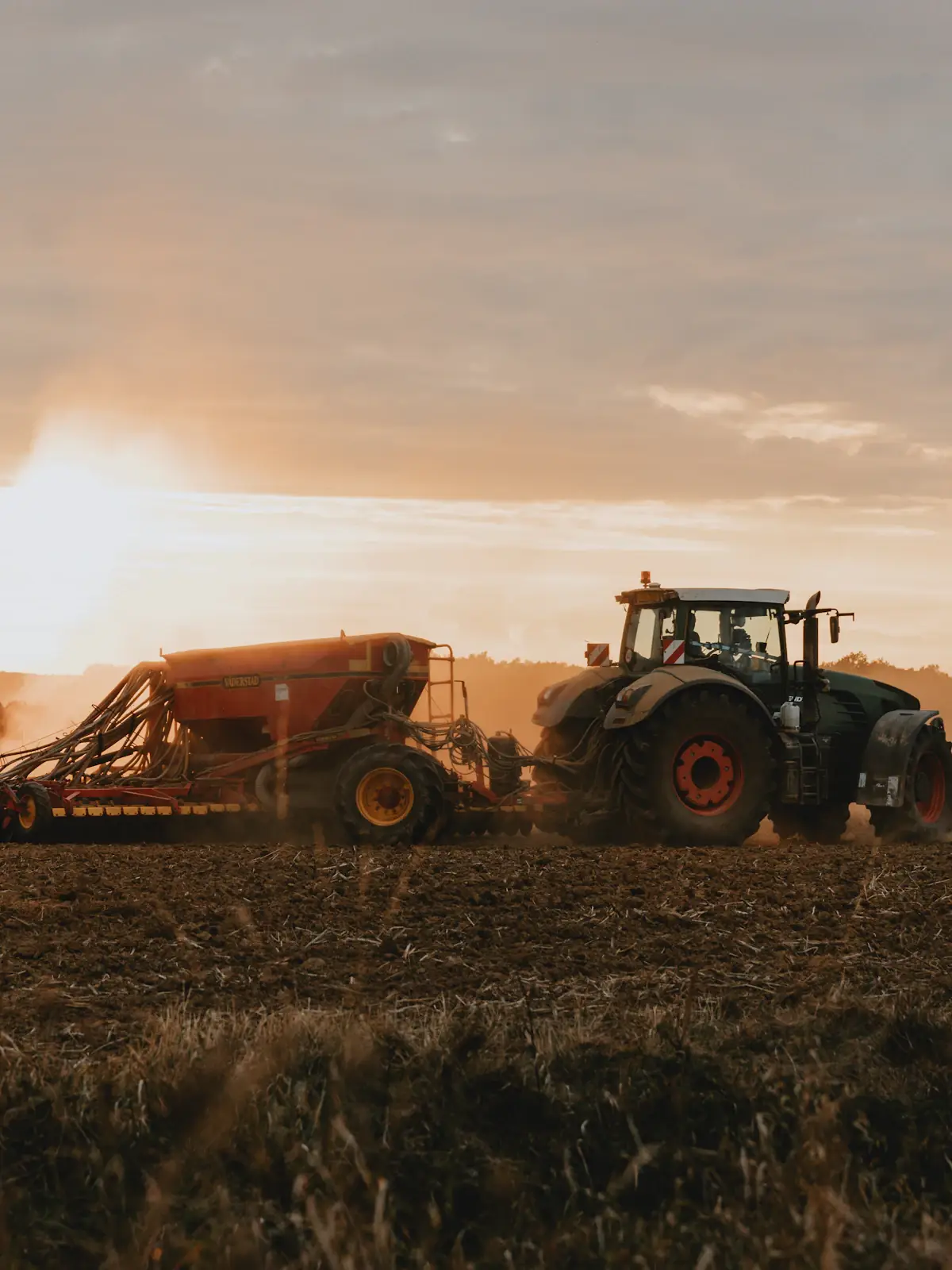 Tractor con sembradora levantando polvo en el campo al atardecer